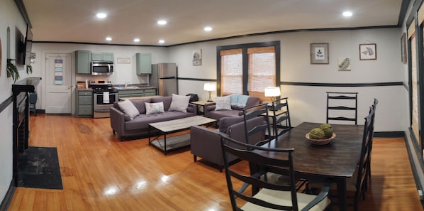 Un espacio habitable compacto con kitchenette, comedor y zona de estar con sofá y sillas.