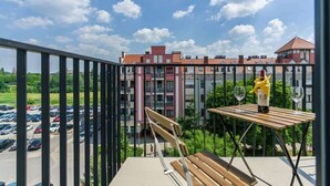 A balcony with a wooden bench and a table, overlooking a parking lot and a building with balconies.