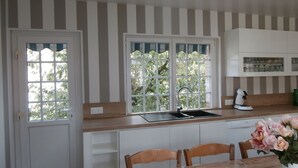 Une cuisine aux murs rayés, une fenêtre donnant sur un paysage verdoyant, un évier, des placards et une table avec des chaises.