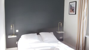 Un lit bien fait dans une pièce dont un mur est peint dans une couleur sombre, une petite table de chevet avec une lampe, et un tableau encadré accroché au mur.