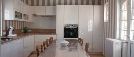 A modern kitchen with a skylight, white cabinets, a wooden dining table, and a large window.