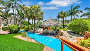 Un patio con un pabellón de techo de paja, una cancha de shuffleboard y palmeras.
