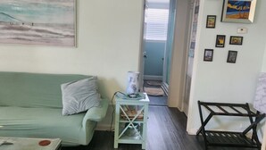 Una sala de estar con un sofá verde, una mesita con una lámpara, un banco de madera y un cuadro en la pared.