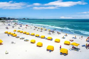 A beach with rows of yellow umbrellas and sun loungers, a clear blue sky, and the ocean.