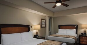 Une chambre d’hôtel avec deux lits, un ventilateur de plafond, une fenêtre avec des rideaux et un tableau encadré au mur.