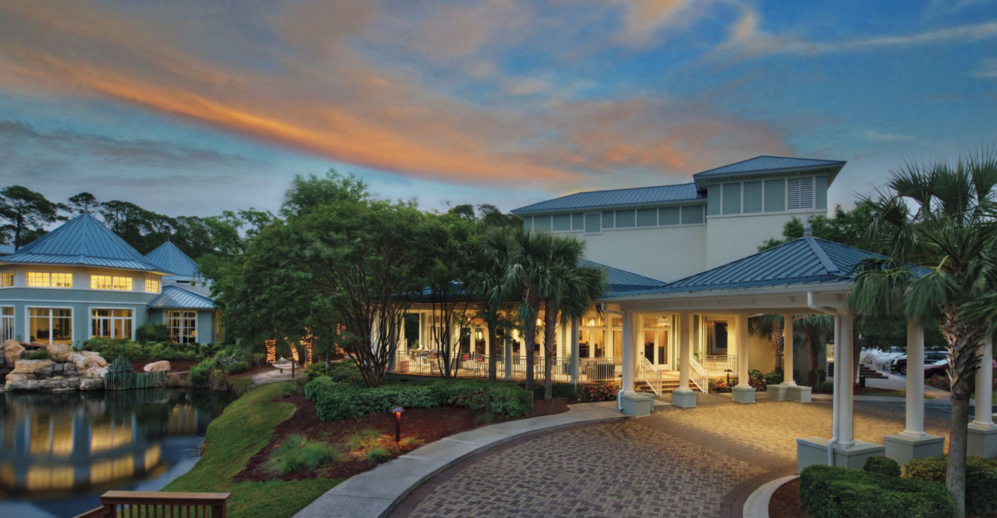 A resort entrance with a covered walkway, a pool, and a large building with a blue roof.