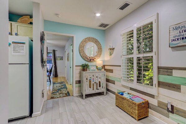 A hallway with a refrigerator, a wicker basket, a cabinet with a mirror, and a window with blinds.