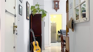 Un couloir avec un porte-guitare en bois, une plante, une horloge et un petit tabouret.