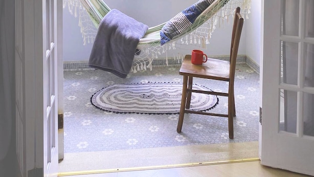 Un fauteuil suspendu avec un coussin à rayures bleues et blanches, une tasse rouge posée sur une table en bois et un tapis tissé sur le sol.