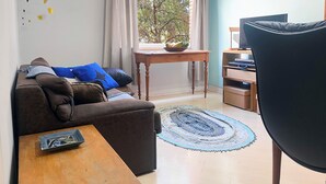Un salon chaleureux avec un canapé marron, une table basse en bois, un tapis bleu et une fenêtre avec des rideaux.