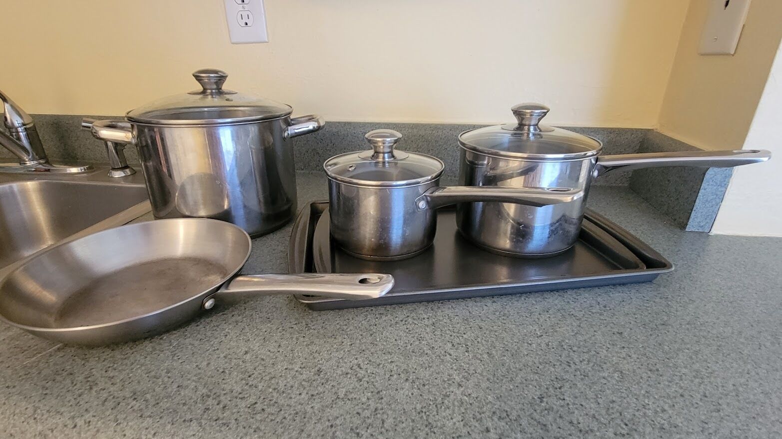 Stainless steel cookware on a kitchen counter, including a frying pan, two pots, and a pan.