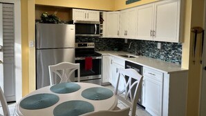 A compact kitchen with white cabinets, a stainless steel refrigerator, a microwave, an oven, and a dishwasher. - Private Beach Living (Cocoa Beach)