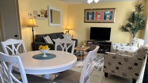 A living room with a round dining table, white chairs, a sofa, a television, and a plant. - Private Beach Living (Cocoa Beach)