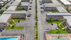 A large parking lot with multiple rows of cars, a swimming pool, tennis courts, and a building with a flat roof. - Private Beach Living (Cocoa Beach)