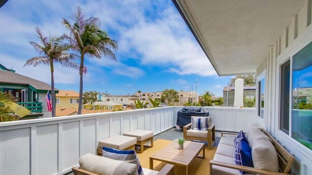Un balcon aménagé avec du mobilier d’extérieur, un barbecue et une vue sur des palmiers et des immeubles.