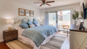 Une chambre à coucher comprenant un lit, des tables de chevet, un ventilateur de plafond, une grande fenêtre et une vue sur l’extérieur.