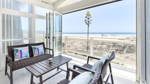 Ein Balkon mit Korbmöbeln, einer Glastür und Blick auf den Strand.