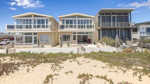 Ein Strandgrundstück mit dreigeschossigen Gebäuden, großen Fenstern und einem Balkon mit Gartenmöbeln.