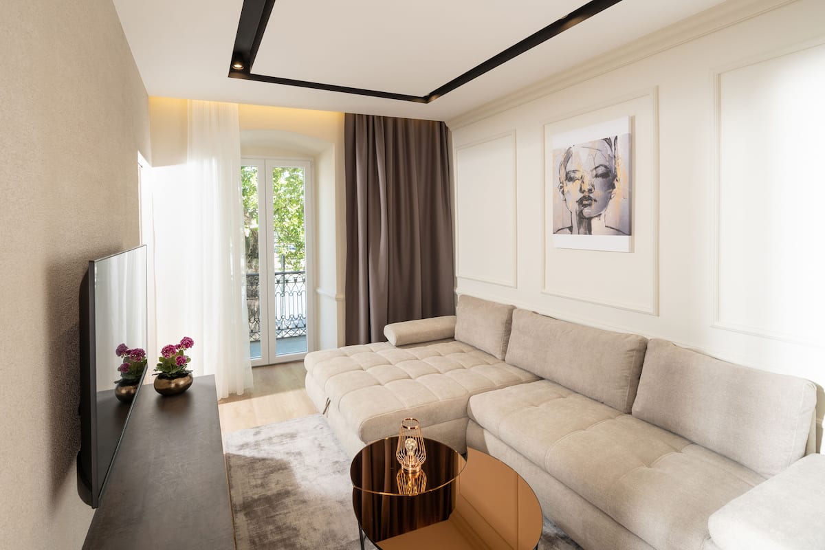 A modern living room with a sectional sofa, a flat-screen TV, a small table with a vase, and a painting on the wall.