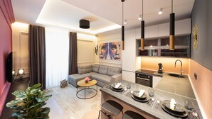 A modern kitchen with a central island, a dining area with a sofa, and a living room with a large painting. - Premium apartments with balcony (Rijeka)