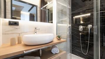 Un baño moderno con un lavamanos grande de color blanco, cabina de ducha con paredes de vidrio y salpicadero de mármol.