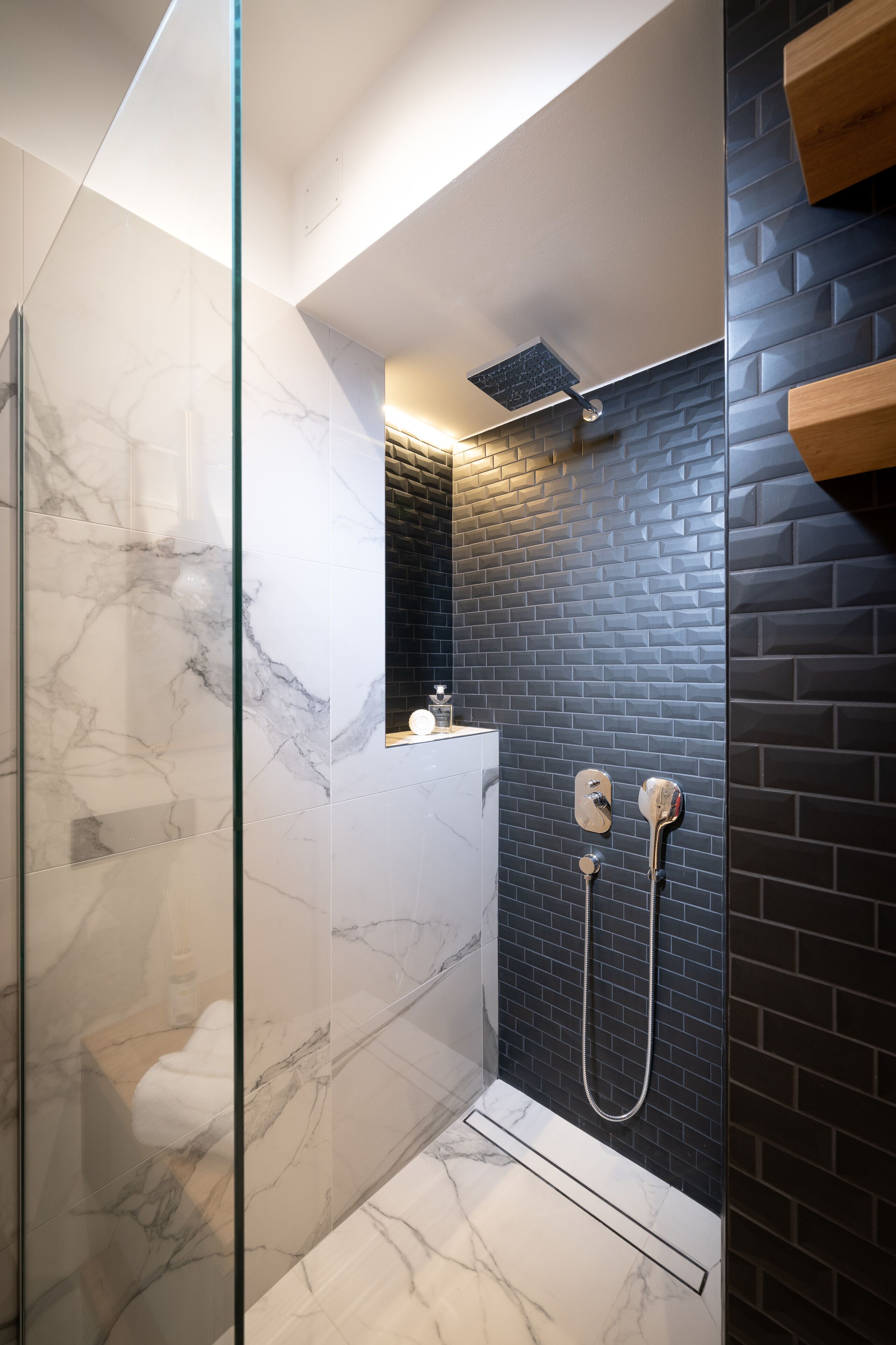 A modern bathroom with a glass shower enclosure, marble flooring, and a black brick wall.
