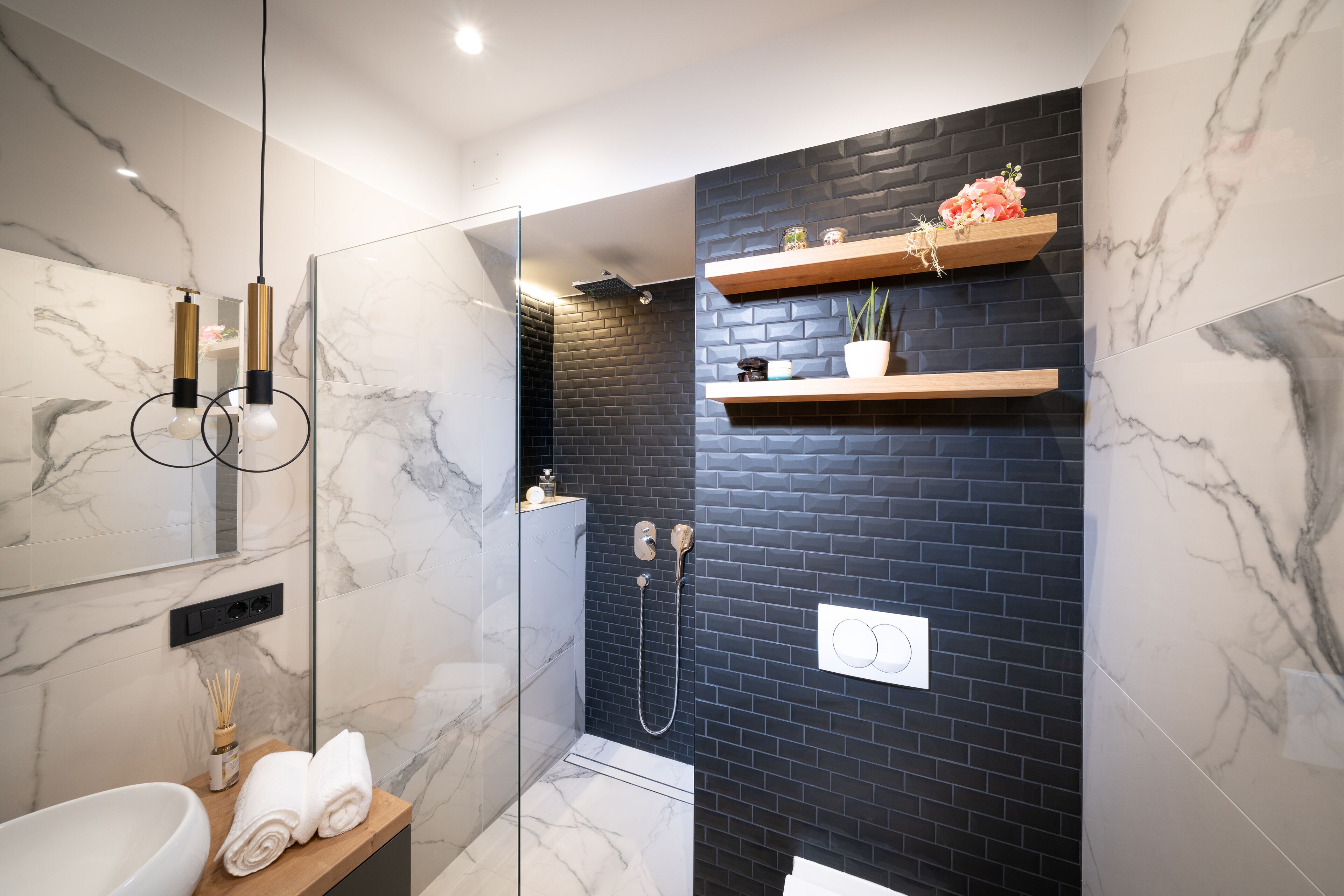 A modern bathroom with a glass-enclosed shower, marble walls, and wooden shelves with decorative items.