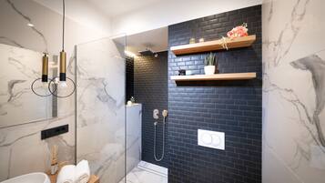 A modern bathroom with a glass-enclosed shower, marble walls, and wooden shelves with decorative items.