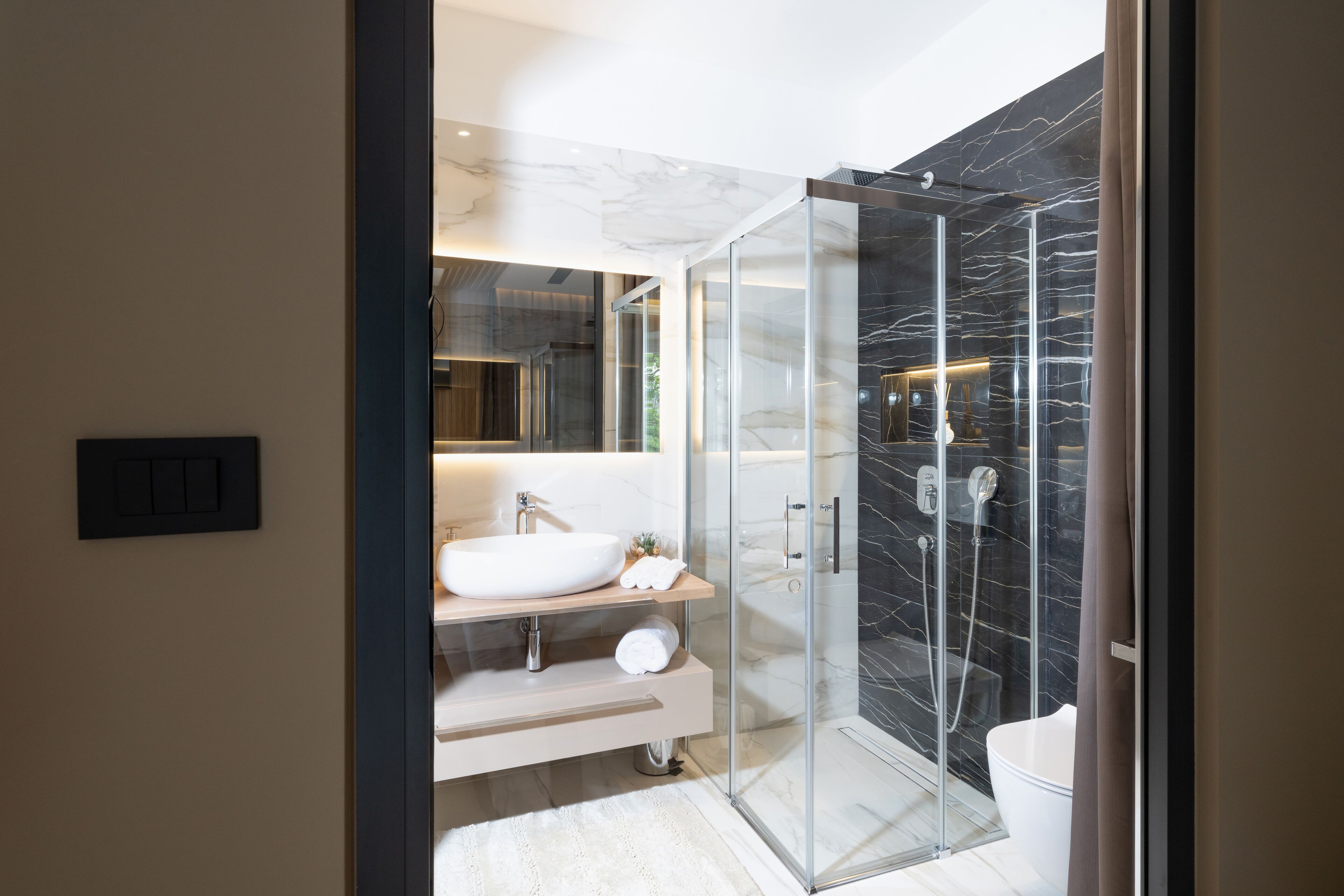 A modern bathroom with a glass-enclosed shower, a white sink, and a marble backsplash.