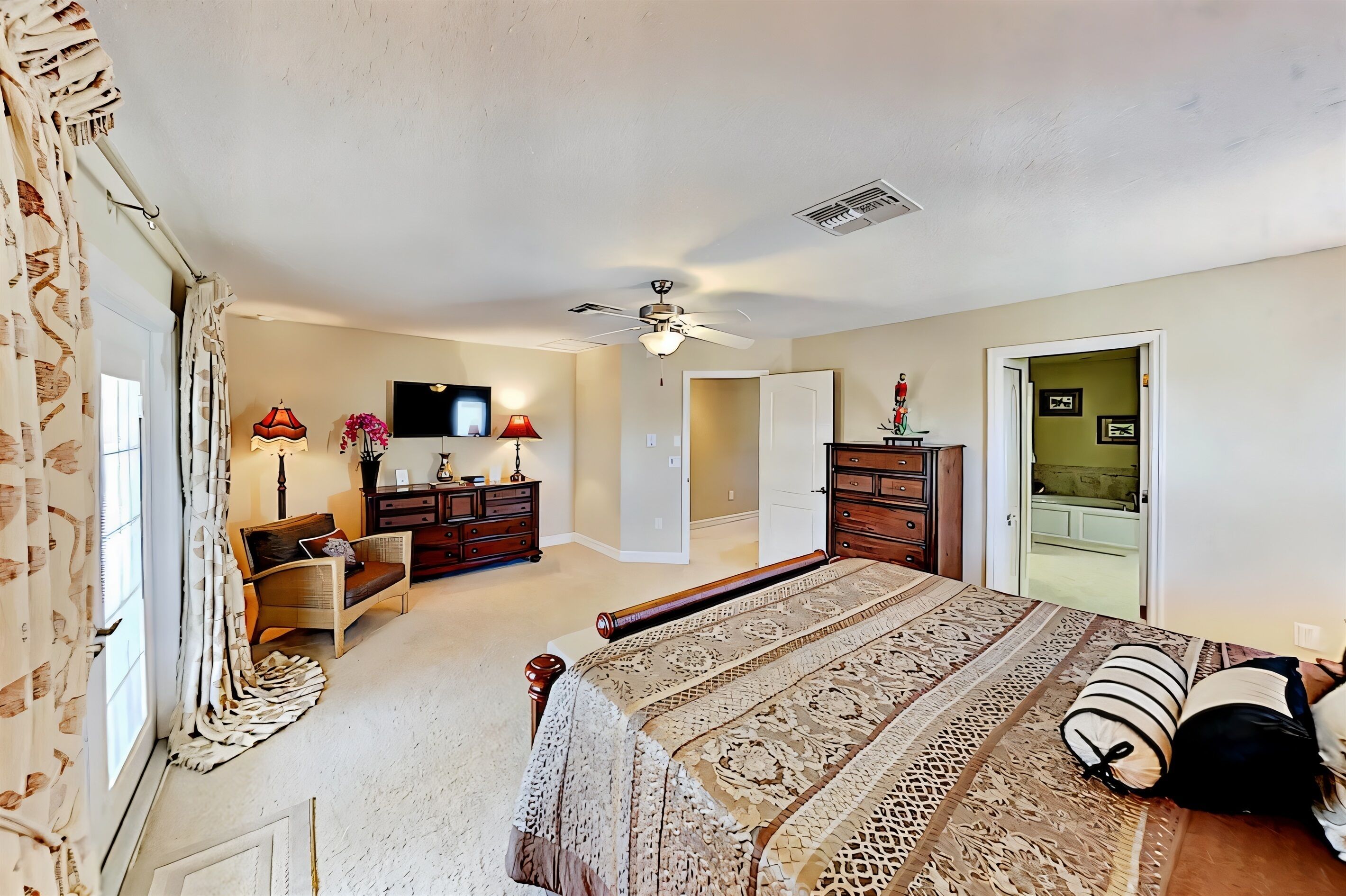 A bedroom with a large bed, a dresser, a chair, a television, and a ceiling fan.