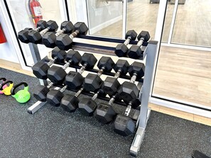 A rack of black dumbbells with a fire extinguisher in the background.