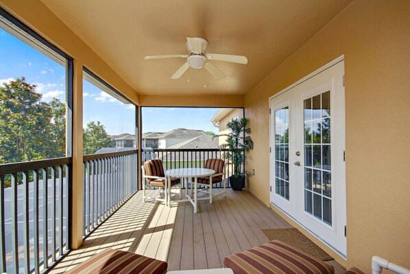 A balcony with a ceiling fan, a table with chairs, and a view of a mountainous landscape.