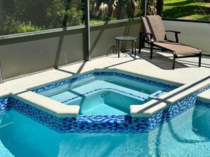 A swimming pool with a tiled edge, a lounge chair, and a small table on a covered deck.