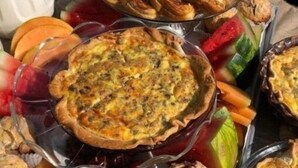 Variedad de productos horneados, como una quiche, muffins y pasteles, acompañados de frutas y verduras frescas.