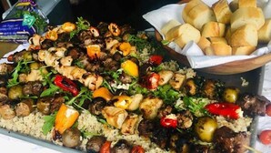 Una presentación de comida con brochetas a la parrilla, arroz y panecillos.