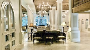 Un vestíbulo amplio con techo alto, candelabros y una zona de estar con mesas y sillas.