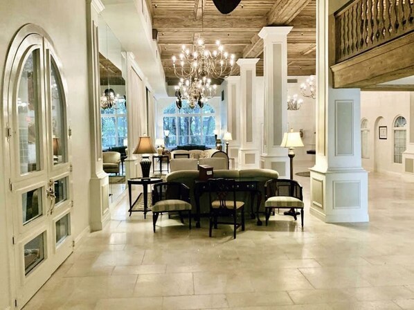 A spacious lobby with a high ceiling, chandeliers, and a seating area with tables and chairs.
