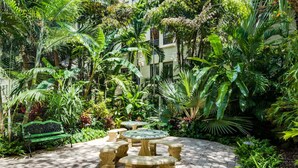 Un jardín con una mesa circular y bancos, rodeado de exuberante follaje.