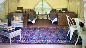Un hébergement sous tente comprenant deux lits, des meubles en osier, un tapis à motifs et une petite table.