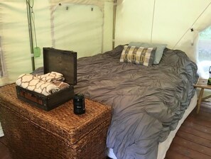 Una carpa con una cama, una maleta y un termo sobre una alfombra tejida.