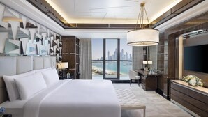 A modern hotel room with a large bed, a desk, a TV, and a view of the city skyline.