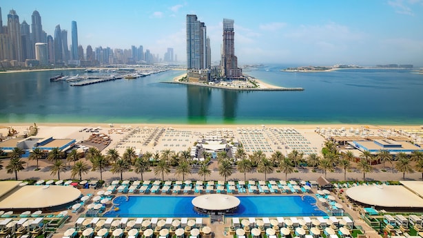 A resort with a large pool, beach area, and views of a city skyline.