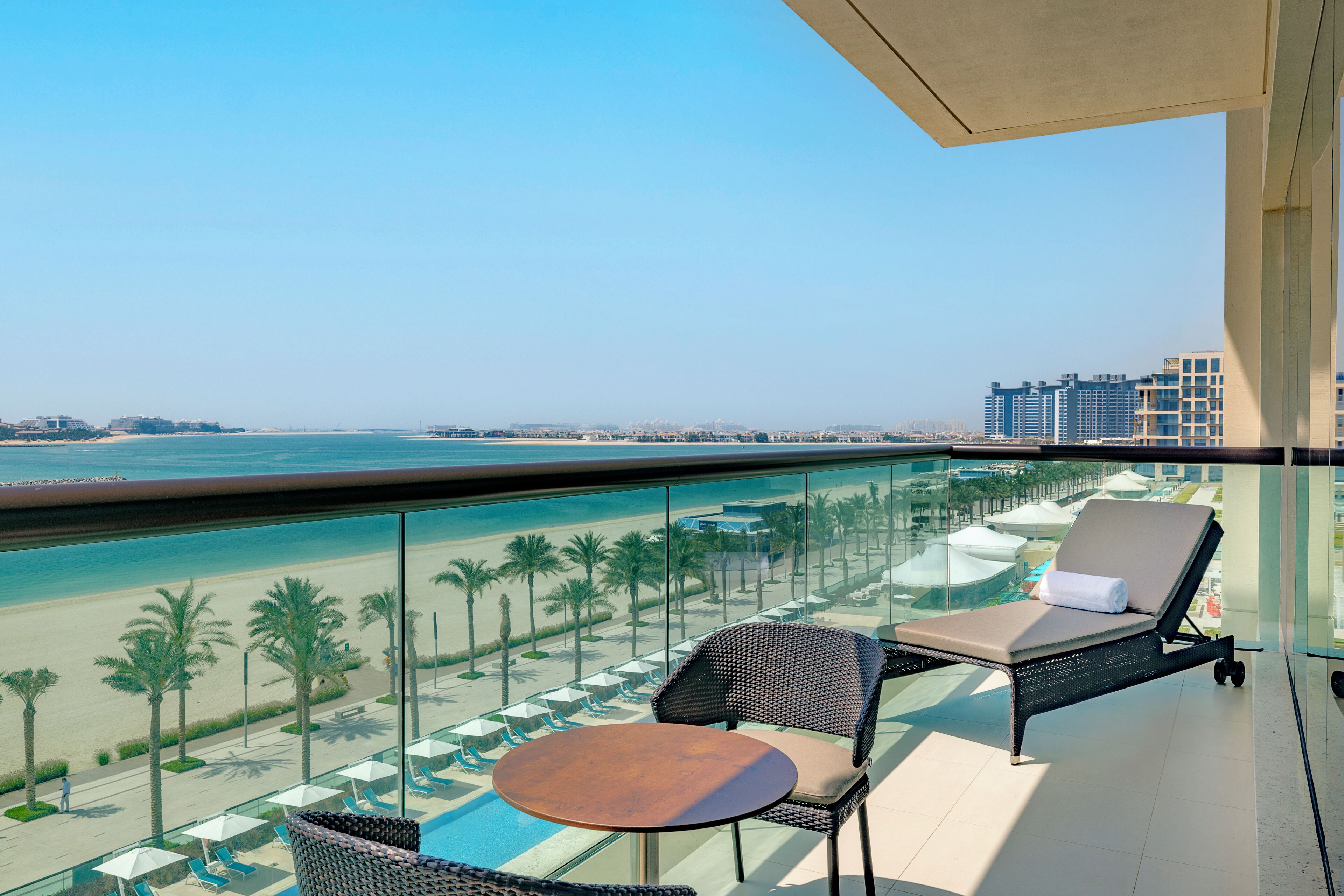 Un balcon avec une piscine, des chaises longues et une table offrant une vue sur la plage et le paysage urbain.