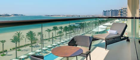 Un balcon avec une piscine, des chaises longues et une table offrant une vue sur la plage et le paysage urbain.