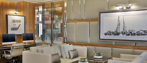 A modern living room with a sofa, armchairs, a coffee table, and a TV. There are bookshelves and a large framed picture on the wall.