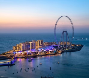 A waterfront cityscape with a prominent Ferris wheel, modern buildings, and a marina with boats.