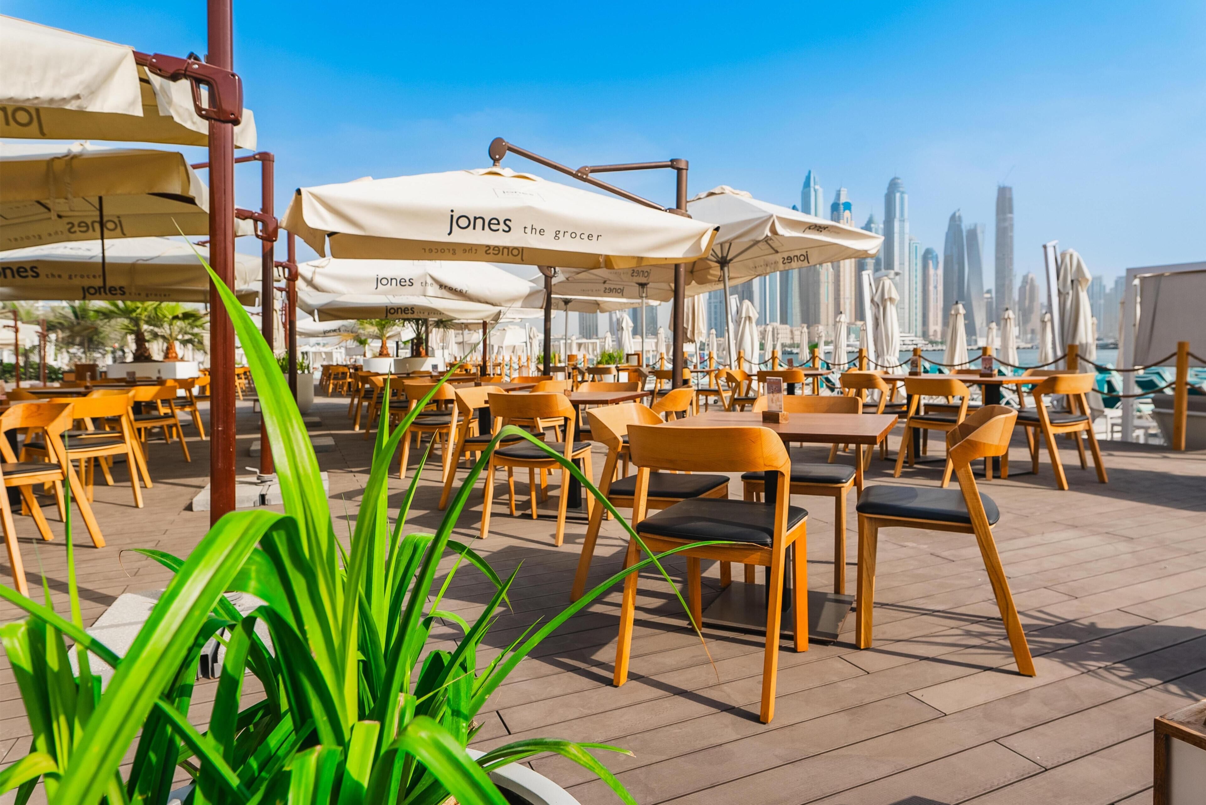 An outdoor seating area with tables and chairs, umbrellas, and a view of a city skyline.