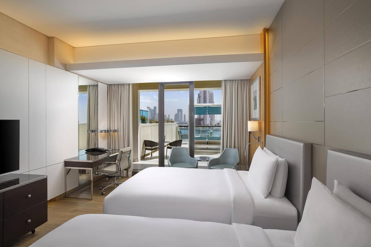 Ein Hotelzimmer mit einem großen Bett, einem Schreibtisch mit Stuhl, einem Fernseher und Blick auf die Stadt.