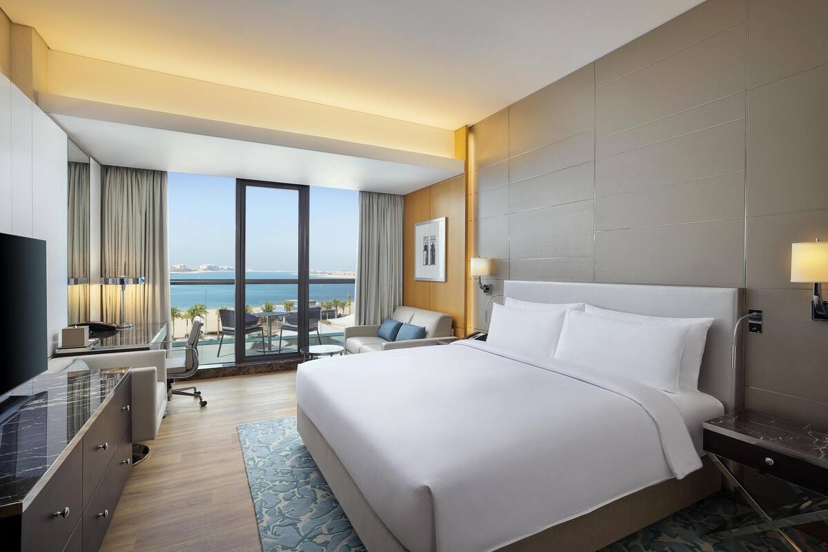 Ein Hotelzimmer mit einem großen Bett, einem Schreibtisch mit Stuhl, einem Fernseher und Blick auf den Ozean.