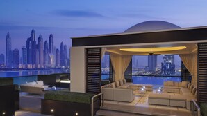 A rooftop lounge with a city skyline view, modern furniture, and a glass barrier.